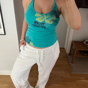 Turkos blommig linnetopp från H&M L.O.G.G. - Säljer en turkos linnetopp från H&M L.O.G.G. med blommigt mönster i gult och mörkblått. Toppen är tight och ärmlös med smala band som knyts runt halsen, perfekt för varma dagar!