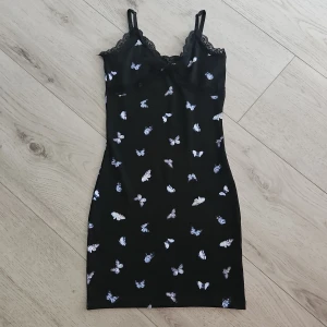 Svart klänning med fjärilsmönster från H&M  - Säljer en svart kortklänning från H&M med blåvita fjärilar och spetsdetaljer vid bysten. Klänningen har smala axelband och är I storlek xs 💞 Aldrig använt 