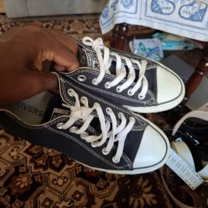 Svarta Converse sneakers med vita detaljer - Klassiska svarta Converse sneakers med vita snören och vit tå. Skorna har låg modell, rund tå och tydliga vita sömmar. Perfekta för en avslappnad stil och passar till det mesta.