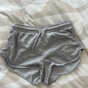 Grå mjuka shorts med dragsko - Grå shorts i mjukt material med elastisk midja och dragsko. De har rundade benslut och fickor på sidorna, perfekta för en avslappnad stil.