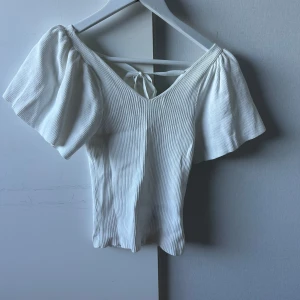 Vit ribbad topp med v-ringning och knyt i ryggen - Säljer en söt vit ribbad topp med v-ringning och vida ärmar. Använt toppen endast en gång🩷