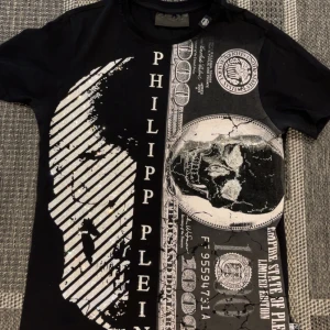 Philipp Plein  - Cool svart t-shirt från Philipp Plein med stort tryck av döskalle och sedlar på framsidan samt logga på ryggen. T-shirten har korta ärmar och är i mjuk bomull. Perfekt för dig som gillar statement-plagg och streetstyle.