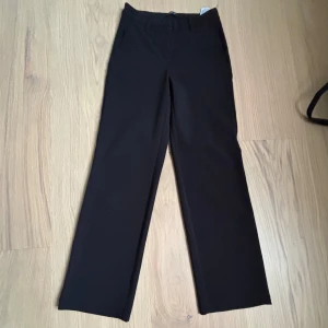 Svarta kostymbyxor  - Snygga svarta kostymbyxor från Vero Moda med klassisk rak passform. Byxorna har hög midja och vida ben, perfekta för en stilren look. Passar till många olika tillfällen och är lätta att matcha med olika toppar och skor.