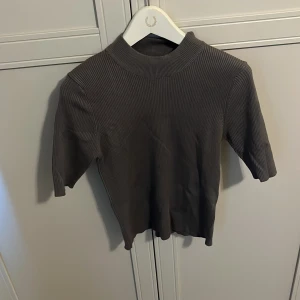 Grå ribbad topp med halv polo - Säljer en grå ribbad topp med halv polokrage och korta ärmar. Toppen har en tight passform och är perfekt att styla till olika outfits. Materialet är stretchigt och bekvämt.