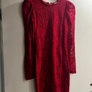 Röd spetsklänning med lång ärm från C - Säljer en röd långärmad klänning från C i storlek XS. Klänningen är täckt av vacker spets och har en figurnära passform. Perfekt för dig som vill sticka ut med en elegant look. Dragkedja bak för enkel påklädning.