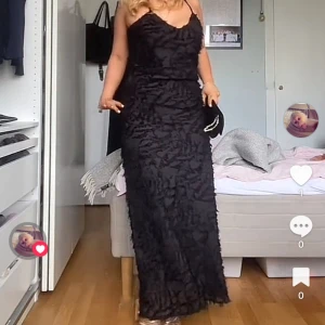Svart balklänning  - Säljer en svart långklänning med smala axelband och volangliknande struktur över hela klänningen. Klänningen har en elegant och figurnära passform, perfekt för festliga tillfällen.