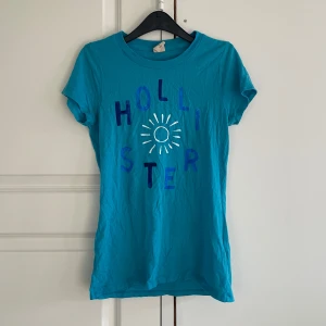 Blå tröja från hollister - En tshirt från hollister perfekt för sommaren, den sitter snyggt! Ganska använd men trycket sitter fortfarande kvar bra! Den är ”nopprig” men det märks knappast. 