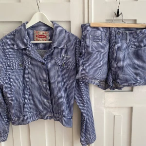 Blårutig set från Radio - Säljer ett blårutigt set från Radio med jacka och shorts. Jackan har långa ärmar och två bröstfickor med knappstängning. Tygmärket och broderad logga ger en unik touch 🐟