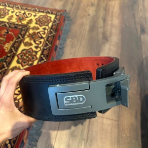 SBD - lyftarbälte - powerlifting  - Perfekt för styrketräning och powerlifting. Bältet är brett och robust, designat för att ge extra stöd vid tunga lyft. Använt under en kort period för två år sedan och bara inte kommit till användning sedan dess. Storleken är mellan XS - S, passade mig vid 60kg (175cm) och även nu vid 70kg (175cm) 