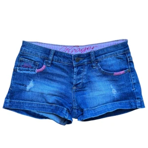 Vintage Blå jeansshorts med rosa broderi  - Jeansshorts med rosa detaljer. Midjemått rakt över: 36 cm. Passar XS-S 