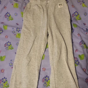 Grå mjukisbyxor med resår från NYC - Säljer ett par ljusgrå mjukisbyxor från NYC med resår i midjan och vid bensluten. Byxorna har en avslappnad passform och är tillverkade i mjukt bomullsmaterial, perfekta för en chill vardagsstil.