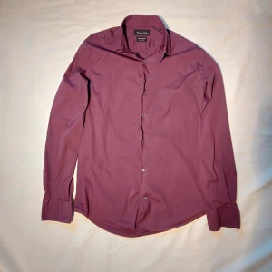 Massimo Dutti skjorta – Storlek M - Stilren långärmad skjorta från Massimo Dutti i en elegant lila nyans. Figursydd/slim fit-modell som sitter snyggt på kroppen. Passar perfekt både till vardags och vid mer uppklädda tillfällen.  ✅ Storlek M ✅ 100 % bomull – mjuk och bekväm mot huden ✅ Klassisk krage och knäppning framtill ✅ Mycket fint skick – inga hål eller fläckar ✅ Från rök- och djurfritt hem  En skjorta med både stil och kvalitet – perfekt för dig som gillar tidlös och sofistikerad look. 