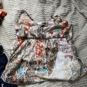 Mönstrad linnetopp från KappAhl - Säljer en luftig linnetopp från KappAhl med smala axelband. Toppen har ett färgstarkt mönster i brunt, vitt, orange och turkost med blommor och blad. Enkel att matcha med jeans eller kjol.