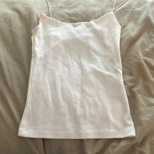 Vit linnetopp från Zara - Säljer en stilren vit linnetopp från Zara med tunna axelband och rak passform. Toppen är enkel och clean, perfekt att matcha med jeans eller kjol. Materialet känns mjukt och lätt, vilket gör den skön att bära under varma dagar.