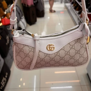 axelväska med GG-mönster - Säljer en snygg axelväska från med klassiskt GG-mönster. Väskan finns i både vitt och svart med guldfärgade detaljer och dragkedja. Tillverkad i skinn och canvas, perfekt storlek för det viktigaste. Justerbar axelrem och ikonisk GG-logga framtill.