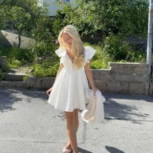 Vit kortklänning med volangärmar - Koller intresset på min supersöta vita kortklänning med djup v-ringning och volangärmar. Klänningen har en luftig passform och är perfekt för varma dagar!! 🍓❣️(Lånad bild). Skriv gärna i DM för fler bilder på självaste klänningen❤️‍🩹