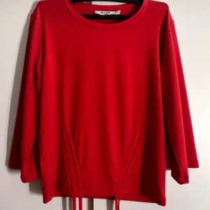 Röd långärmad tröja från NA-KD - Snygg röd långärmad tröja från NA-KD med rund halsringning och dragsko-detaljer nertill. Tröjan är i mjuk bomull och har en clean look som är lätt att styla. Perfekt för dig som gillar enkel men trendig stil.