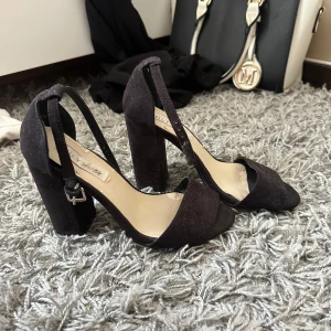 Svarta chunky klackpumps från NLY Shoes - Snygga svarta pumps med bred klack och öppen tå från NLY Shoes. Skorna har en justerbar rem runt ankeln och är klädda i mockaliknande material. Perfekta för att lyfta din outfit med en trendig och stilren vibe.