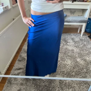 Blå satinkjol med dragkedja - Säljer en lång, glansig blå kjol i satinliknande material. Kjolen har en figurnära passform och stängs med dragkedja. Den skrynklar sig vid sidan. Men är super söt💕