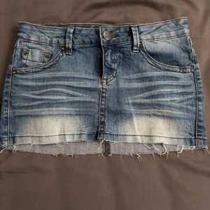 Blå jeanskjol från MNG Jeans, strl 34 - Snygg blå jeanskjol från MNG Jeans i storlek 34. Kjolen har slitna detaljer, rå kant nertill och klassiska fem fickor. Perfekt för en chill och trendig look. Midjehög passform och cool tvättad effekt gör den superenkel att styla.