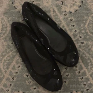 Svarta ballerinaskor med paljetter - Snygga svarta ballerinaskor täckta med glittriga paljetter och en söt rosett framtill. Skorna har rund tå och platt sula, perfekta för dig som vill ha något stilrent men ändå med lite extra bling.