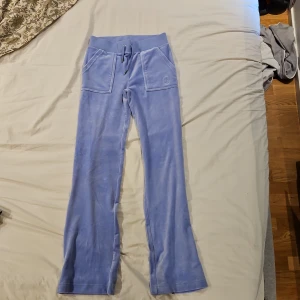 Nya ljusblå velourbyxor Juicy Couture XS - Supermjuka ljusblå velourbyxor från Juicy Couture med bred resår i midjan och snörning. Byxorna har raka ben, stora fickor fram och broderad JC-logga på ena fickan. Perfekta för en chill och trendig look. Enbart provade.