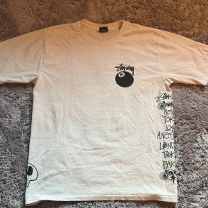 Vit Stüssy t-shirt med tryck, M - Vit t-shirt från Stüssy med stora grafiska tryck på både fram- och baksida. Flera färgglada Stüssy-loggor, döskallar och 8-ball motiv. Tvärskön passform