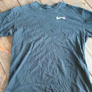 Svart Nike SB t-shirt med tryck - Svart t-shirt från Nike SB i bomull med coolt tryck av en gul hund på moln och rosa Nike-logga på ryggen. Klassisk passform, rund hals och korta ärmar. Liten Nike SB-logga framtill. Perfekt för dig som gillar streetwear och snygga prints.