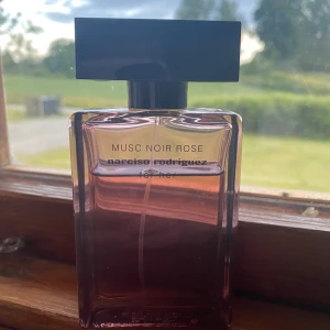 Musc Noir Rose parfym Narciso Rodriguez - Musc Noir Rose från Narciso Rodriguez for her är en elegant parfym i en rektangulär glasflaska med mjukt rosa toning och svart fyrkantigt lock. Doften är feminin och modern, perfekt för dig som gillar blommiga och sensuella toner.