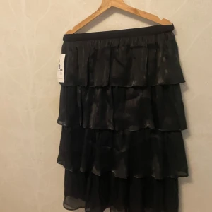 Hell ny Svart volangkjol med resårmidja - Säljer hell ny,Snygg svart långkjol med flera lager volanger och bred resår i midjan. Kjolen har en lätt glansig yta och faller riktigt fint. Perfekt för dig som vill ha en statement piece i garderoben. Storlek M