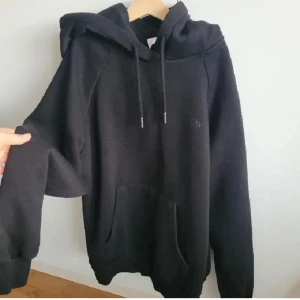 Svart hoodie från ICIW - Svart hoodie med stor huva, snörning och magficka. Klassisk och enkel design med långa ärmar och ribbade muddar. Perfekt för en avslappnad stil och passar till det mesta. Materialet känns mjukt och bekvämt.