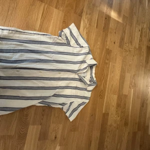 Randig skjorta från Les Deux - Snygg kortärmad skjorta från Les Deux i vitt med blåa ränder. Skjortan har klassisk krage, knäppning framtill och avslappnad passform. 