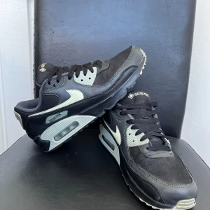Nike Air Max 90 Gore-Tex svart/vit - Nike Air Max 90 Gore-Tex sneakers i svart och vitt med klassisk siluett, synlig Air Max-dämpning och robust mesh- och skinnöverdel. Swoosh-logga i vitt och detaljer i grått. Perfekta för dig som vill ha stil och funktion i ett.