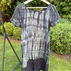 Svartgrå batikklänning från Silke - Unik kortklänning från Silke i svart och grått batikmönster. Tillverkad i tunt silke med korta ärmar och rund halsringning. Baksidan har knappar upptill för en extra detalj. Perfekt för dig som gillar en avslappnad men cool stil.