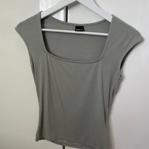 Ljusgrå/grön linnetopp från Gina Tricot - Säljer en stilren ljusgrå/grön linnetopp från Gina Tricot. Toppen har en fyrkantig ringning och är ärmlös, vilket ger en clean och modern look. Perfekt att matcha med jeans eller kjol för en enkel men snygg outfit.