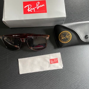 Ray-Ban Wayfarer solglasögon brun - Snygga Ray-Ban Wayfarer solglasögon i brun transparent plast med mörka glas. Klassisk fyrkantig form och ikoniska detaljer vid bågens hörn. Kommer med originalfodral, putsduk och box. Perfekt accessoar för soliga dagar.