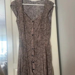  leopardmönstrad klänning - Snygg  klänning med svart leopardmönster och knappar framtill. Modellen är kortärmad med v-ringning och har en avslappnad passform. Perfekt för dig som gillar djurmönster och vill sticka ut lite extra.