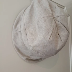 Beige keps i linne-look - Snygg beige keps med avslappnad passform och coola sömdetaljer. Tillverkad i ett linne-liknande material med vit mesh på insidan för extra ventilation. Perfekt för dig som vill ha en stilren och luftig huvudbonad.