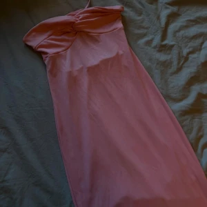 Rosa axelbandslös långklänning - Supersnygg rosa långklänning med axelbandslös design och twistad detalj vid bysten. Klänningen har en figurnära passform och är perfekt för dig som vill sticka ut. Mjuk och stretchig känsla, passar till många tillfällen. Storlek M