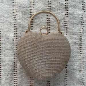 Glittrig hjärtformad kuvertväska - Supersöt hjärtformad kuvertväska i glittrigt guld med ett handtag och en ringformad stängning dekorerad med strass. Perfekt accessoar när du vill sticka ut och addera lite extra bling till din outfit.