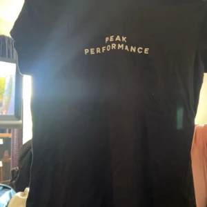 Svart Peak Performance t-shirt S - Svart t-shirt från Peak Performance med vit logga tryckt på bröstet. Klassisk passform och rund halsringning, perfekt för en clean och sportig look. Tillverkad i mjuk bomull som känns skön mot huden.