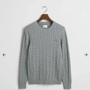 Grå stickad tröja från GANT - Snygg grå stickad tröja från GANT med rund halsringning och logga på bröstet. Tröjan har en en klassisk look och kostar orginalt 1600kr. Perfekt för dig som gillar stickade tröjor. Meddela mig för mer frågor🤩