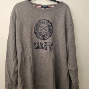 Tröja Gant  - Grå herrtröja med tryck. Litet hål i nacken, därav priset. Se bild.