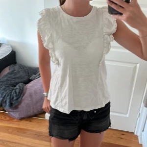 Vit volangblus från GAP Kids - Passar på mig, 169. Supersöt vit blus från GAP Kids i bomull med volangdetaljer längs axlarna. Ärmlös modell med rund halsringning och lätt, luftig känsla. Perfekt för dig som gillar en feminin och enkel stil med extra touch av volanger.