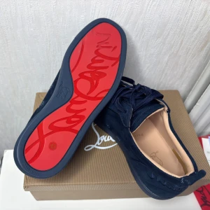 Mörkblå mocka sneakers från Louboutin - Snygga mörkblå sneakers från Christian Louboutin i mjuk mocka med klassisk röd sula och broderad logga på hälen. Skorna har rund tå, platt sula och snörning. Perfekta för dig som vill sticka ut med exklusiv design och lyxiga detaljer.