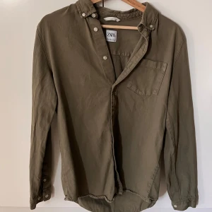 Olivgrön skjorta från Zara - Stilren olivgrön skjorta från Zara med klassisk krage och bröstficka. Skjortan har knappar framtill och långa ärmar med knapp vid ärmslut. Perfekt för en avslappnad men snygg look.