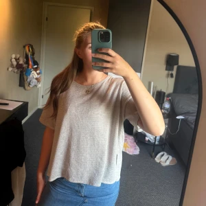 Ljusgrå croppad topp med glittrig känsla - Säljer en ljusgrå croppad topp med korta ärmar och rund hals. Tyget har en diskret glittrig effekt som ger en snygg touch. Passformen är loose och toppen är perfekt att styla med jeans eller kjol för en chill look.