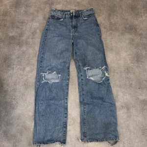 Levi's 501 blå jeans med slitna knän - Klassiska Levi's 501 jeans i ljusblå denim med raka ben och hög midja. Snygga slitningar och hål på båda knäna samt fransiga benslut för en avslappnad och trendig look. Perfekta för dig som gillar vintage vibe och streetstyle. Nedre delen av byxorna har slitits sönder pga för långa för mig 
