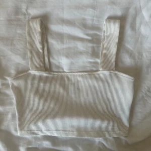 Croppad vit ribbad linne - Säljer en stilren vit ribbad linnetopp med breda axelband. Toppen är croppad och har en enkel, rak passform som passar perfekt till jeans eller kjol. Materialet är mjukt och stretchigt för en bekväm känsla hela dagen