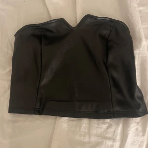 Svart tubtopp i skinnimitation - Säljer en svart tubtopp från Amisu i skinnimitation. Dragkedja i sidan gör den enkel att ta på och av. Väldigt fint skick ❤️